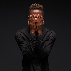 Emotional portrait of a young African man in black clothing against a dark background. Studio photography.