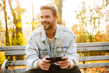 Obraz premium Handsome young man sitting on a bench in the autumn park