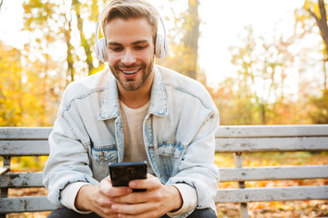 Fototapeta premium Handsome young man sitting on a bench in the autumn park