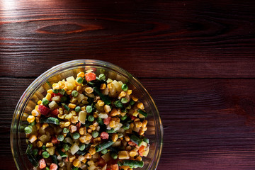 Frozen different vegetables in a glass plate on a wooden background.