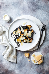 Black squid ink spaghetti with king oyster mushrooms, cream sauce and parmesan on white plate.