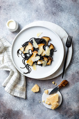 Black squid ink spaghetti with king oyster mushrooms, cream sauce and parmesan on white plate.