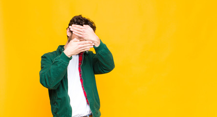 young crazy bearded man covering face with both hands saying no to the camera! refusing pictures or...