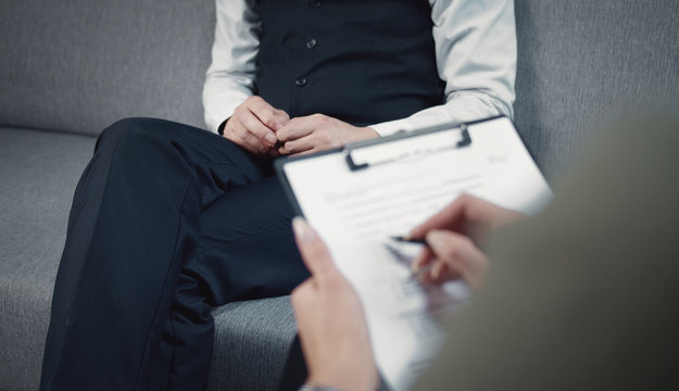 Cropped image of psychiatrist making notes during therapy session with patient, client's torso focus