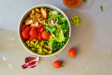 Vegan Bowl. Vegetable salad with avocado, tomatoes, herbs, iceberg lettuce, lettuce, sweet and sour sauce and yogurt. Healthy vegetarian lunch. Salad in a gray clay bowl on a gray concrete background.