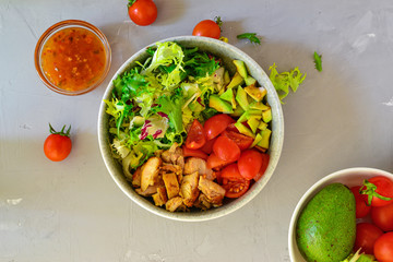 Vegan Bowl. Vegetable salad with avocado, tomatoes, herbs, iceberg lettuce, lettuce, sweet and sour sauce and yogurt. Healthy vegetarian lunch. Salad in a gray clay bowl on a gray concrete background.