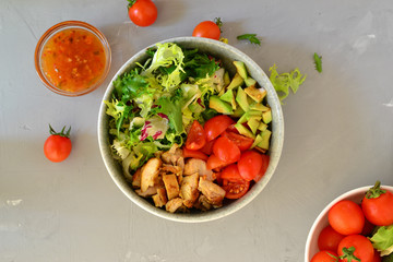 Vegan Bowl. Vegetable salad with avocado, tomatoes, herbs, iceberg lettuce, lettuce, sweet and sour sauce and yogurt. Healthy vegetarian lunch. Salad in a gray clay bowl on a gray concrete background.