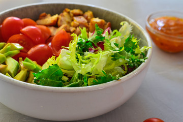 Vegan Bowl. Vegetable salad with avocado, tomatoes, herbs, iceberg lettuce, lettuce, sweet and sour sauce and yogurt. Healthy vegetarian lunch. Salad in a gray clay bowl on a gray concrete background.