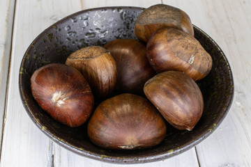 Group of seven whole edible brown chestnut in glazed bowl on white wood