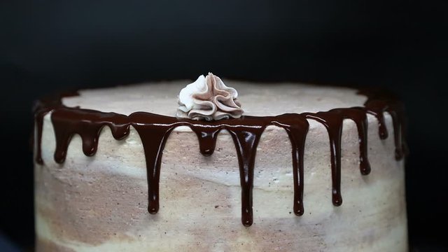 Decorating cake with cream. Beautiful tasty cake with chocolate icing is decorated with cream using pastry nozzle.