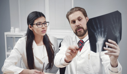 Two doctors discussing patient's hands xray image, preceptor showing roentgenogram details to intern