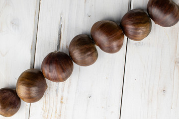 Group of seven whole edible brown chestnut diagonal flatlay on white wood