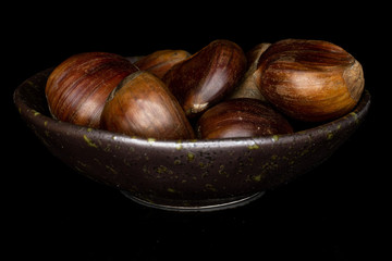 Lot of whole edible brown chestnut in glazed bowl isolated on black glass