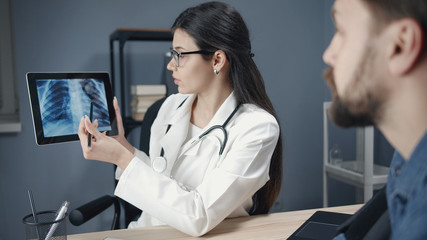 Young woman doc explaining chest x-ray results to male patient showing it on tablet