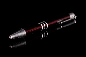 One whole dark red writing ballpoint pen isolated on black glass