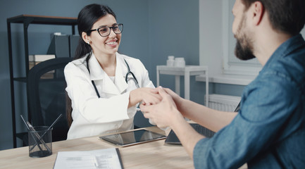 Smiling female doctor shaking hands with satisfied male patient, trust and medical ethics concept