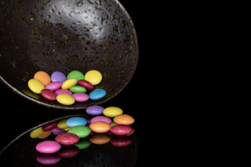 Lot of whole sweet colourful candy in glazed bowl isolated on black glass