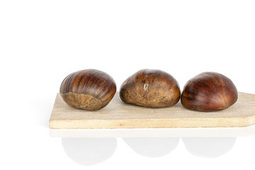 Group of three whole edible brown chestnut on wooden cutting board isolated on white background