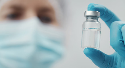 Cropped shot of doctor holding transparent glass medical vial in hand, focus on bottle - obrazy, fototapety, plakaty