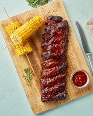 Barbecue pork ribs. Slow cooking recipe. Whole pickled roasted pork meat with red sauce and corn on cutting board