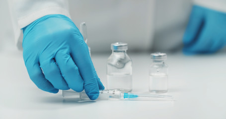 Hand putting filled syringe on table next to medical glass vials with transparent liquid, cropped