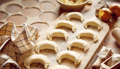 Raw dumplings with cheese and potato filling prepared for cooking on a wooden board, close-up view. 