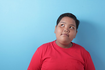 Portrait of cute fat Asian boy looking up, thinking something and smile, finding good idea