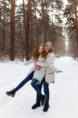 Fototapeta premium Happy lovers a guy and a girl who love each other hug, kiss, laugh, rage and walk in warm jackets in winter against the background of a snowy forest, a friendly family fun walk
