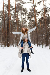 Happy lovers a guy and a girl who love each other hug, kiss, laugh, rage and walk in warm jackets in winter against the background of a snowy forest, a friendly family fun walk