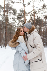 Happy lovers a guy and a girl who love each other hug, kiss, laugh, rage and walk in warm jackets in winter against the background of a snowy forest, a friendly family fun walk