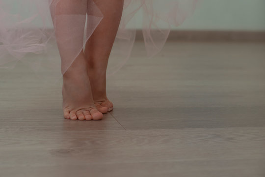 legs of a little girl on tiptoe in a long light pink skirt of transparent organza are on the parquet. little ballerina