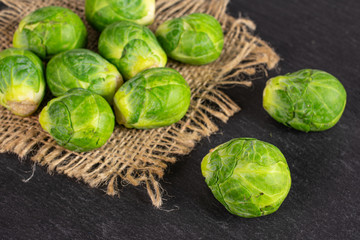 Lot of whole fresh green brussels sprout on natural sackcloth on grey stone