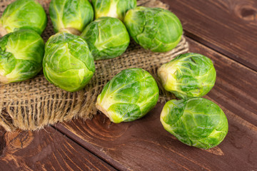 Lot of whole fresh green brussels sprout on natural sackcloth on brown wood