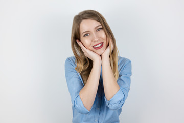 young beatuiful blond smiling woman looks satisfied touching her face with both hands standing on isolated white background, body language