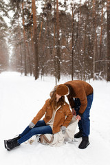 Happy lovers a guy and a girl who love each other hug, kiss, laugh, rage and walk in warm jackets in winter against the background of a snowy forest, a friendly family fun walk