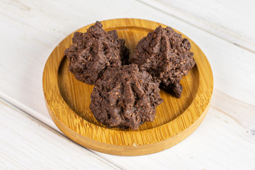 Group of three whole homemade brown coconut cocoa biscuit on bamboo coaster on white wood