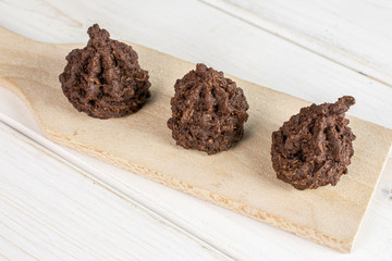Group of three whole homemade brown coconut cocoa biscuit on small wooden cutting board on white wood