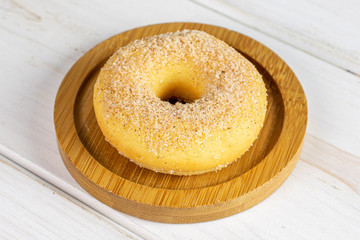 One whole sweet golden mini cinnamon donut on bamboo coaster on white wood