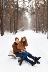 Fototapeta premium Happy lovers a guy and a girl who love each other hug, kiss, laugh, rage and walk in warm jackets in winter against the background of a snowy forest, a friendly family fun walk