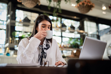 Attractive caucasian elegant brunette sitting in cafe, drinking coffee. On table is laptop.