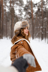 Fototapeta premium Happy lovers a guy and a girl who love each other hug, kiss, laugh, rage and walk in warm jackets in winter against the background of a snowy forest, a friendly family fun walk