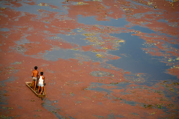 small boat and men on red algae covered lake