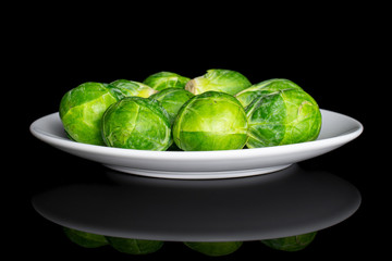 Lot of whole fresh green brussels sprout on white ceramic plate isolated on black glass