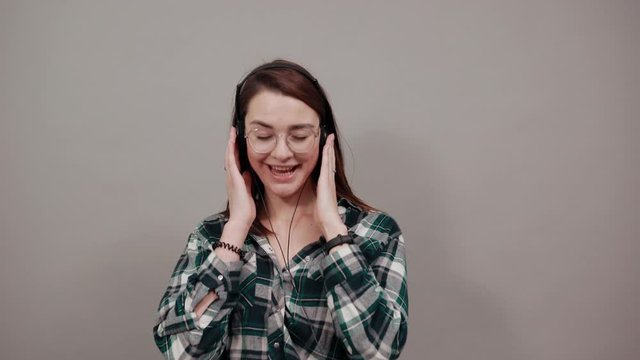 Young brunette girl blue green in checked shirt on grey background happy woman listening to music with headphones