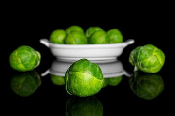 Group of nine whole fresh green brussels sprout in white oval ceramic bowl isolated on black glass