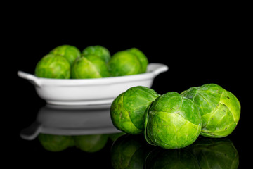 Group of nine whole fresh green brussels sprout in white oval ceramic bowl isolated on black glass
