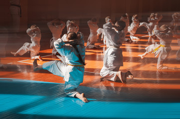 A teenage girl with a yellow belt in a karate class trains a direct kick. Beautiful morning light. Oriental martial arts. Children's training. No faces. With place for text. © Uladzimir