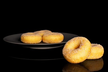Group of five whole sweet golden mini cinnamon donut on gray ceramic plate isolated on black glass