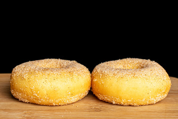 Group of two whole sweet golden mini cinnamon donut on bamboo cutting board isolated on black glass