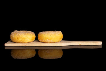 Group of two whole sweet golden mini cinnamon donut on small wooden cutting board isolated on black glass